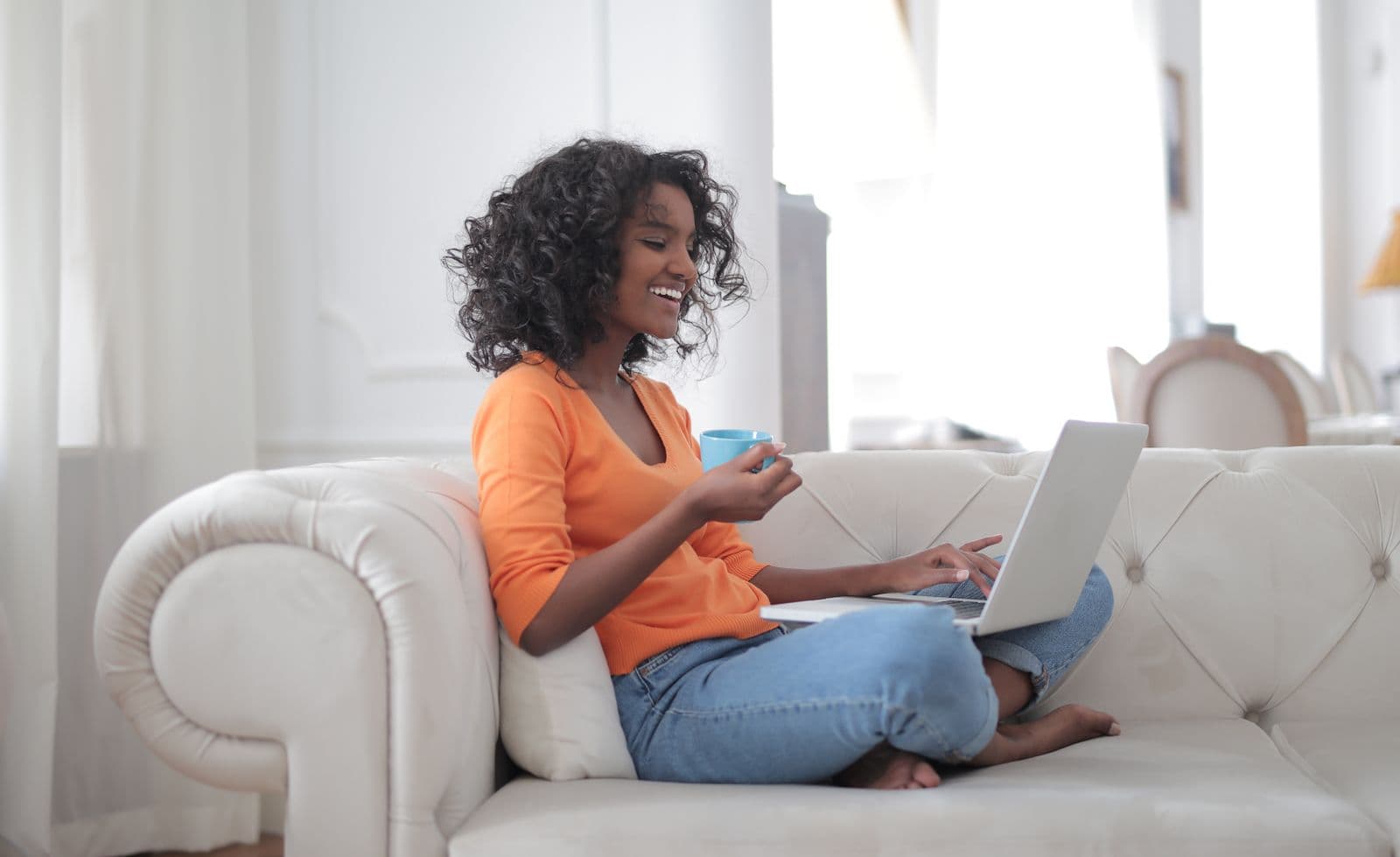 Étudiante souriante suivant ses cours en ligne depuis son ordinateur portable, chez elle